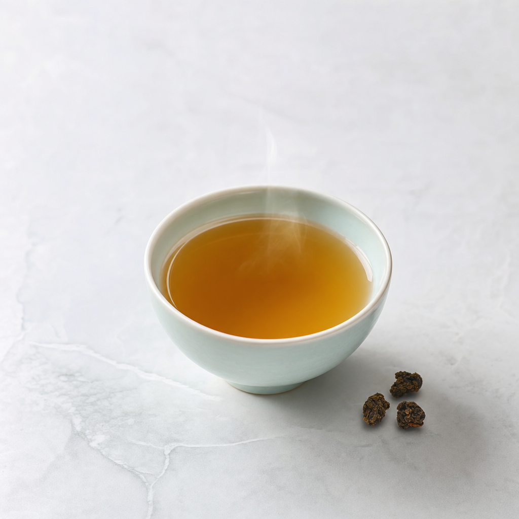 A small pale celadon cup of clear golden-brown Ember Crown Signature Dark Oolong on a pale grey stone surface