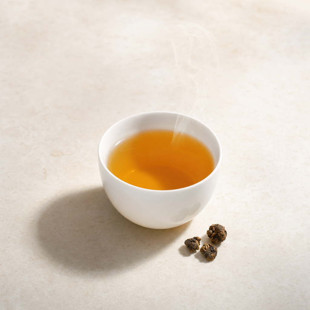 A small white porcelain cup of clear golden-brown Ember Crown Reserve Dark Oolong on a pale stone surface