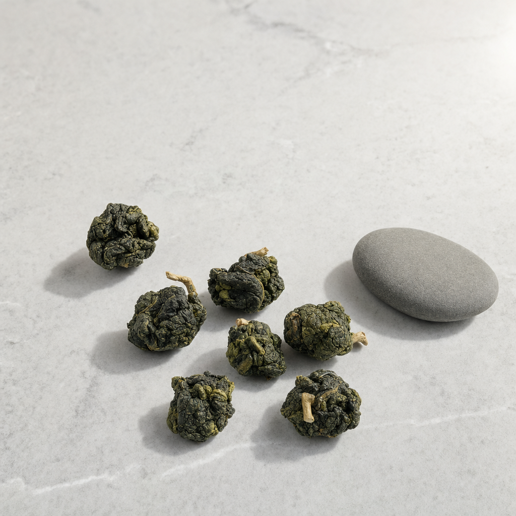A small group of hand-rolled Mountain Crown Reserve Oolong pellets with visible stem fragments and a smooth river stone on a whitish-grey marble surface