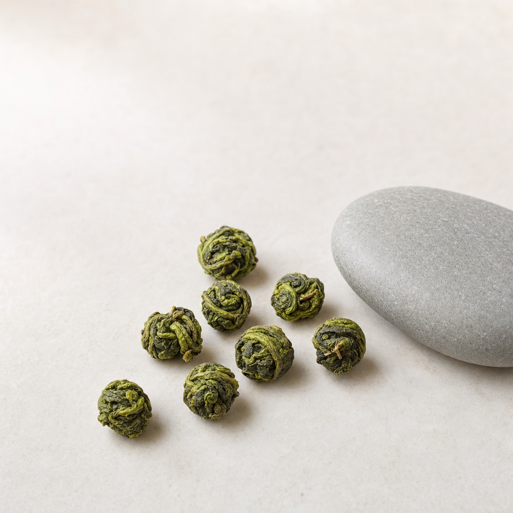 A small arrangement of middle-pluck Cloud Bridge Oolong pellets on a pale stone surface — pellets that read visually between a premium tight roll and a broader-leaf loose roll