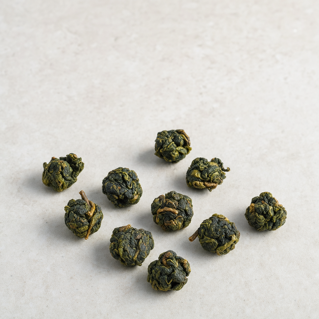 A small relaxed scatter of tightly-rolled jade-green Tie Guan Yin oolong nuggets on a pale stone surface