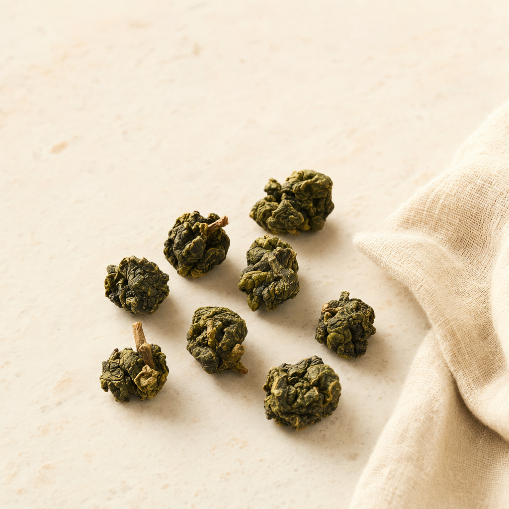 A small arrangement of rolled Mountain Crown Select Oolong pellets on a warm cream stone surface beside a soft fold of linen