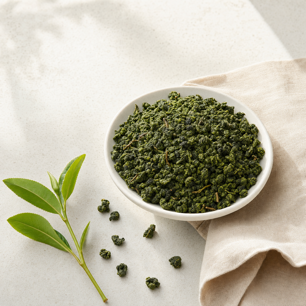 Cloud Bridge Oolong loose-leaf rolled jade pellets in a wide shallow stoneware bowl on a pale stone surface, with a larger fresh tea sprig and a folded linen napkin