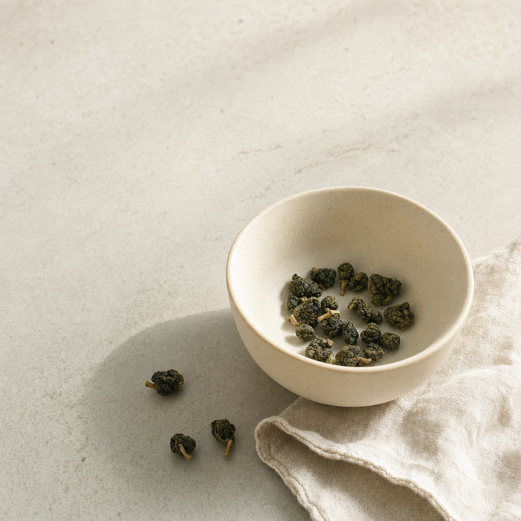 Mountain Crown Select Oolong loose-leaf rolled jade pellets in a small cream stoneware cup on a bright stone surface, with a soft folded linen