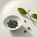 Ember Crown Signature Dark Oolong roasted rolled pellets in a pale celadon bowl on a bright stone surface, with a fresh tea sprig