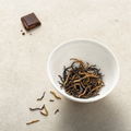Yunnan Crown Reserve Black Tea loose wiry dark leaf dense with fat golden buds in a small white porcelain bowl on a bright stone surface