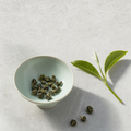 Mountain Crown Signature Oolong loose-leaf rolled jade pellets in a pale celadon bowl on a bright stone surface, with a fresh one-bud-two-leaves tea sprig