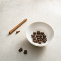 Ember Crown Reserve Dark Oolong roasted rolled pellets in a small white porcelain bowl on a bright stone surface, with a cinnamon-stick accent