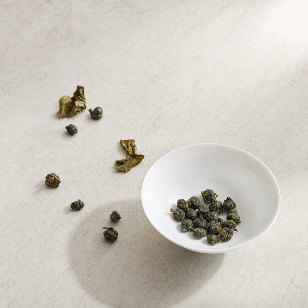 Tightly rolled Tie Guan Yin oolong nuggets in a small white porcelain bowl on a bright stone surface