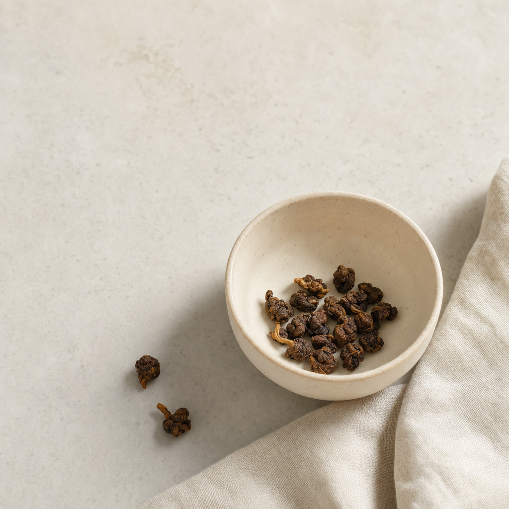 Ember Crown Select Dark Oolong roasted rolled pellets in a small cream stoneware cup on a bright stone surface, with a soft folded linen